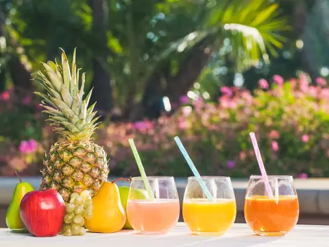 Vasos de refrescos naturales de frutas junto a una piña y frutas frescas.