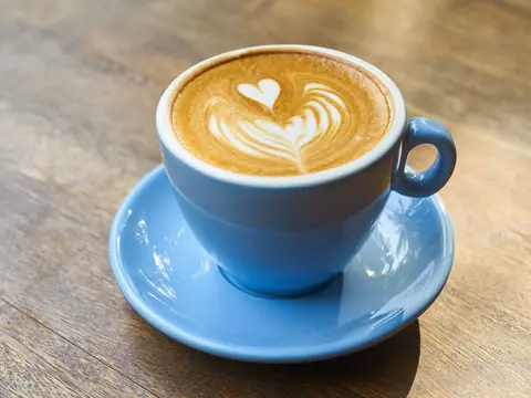 Taza de capuchino con arte latte sobre una mesa de madera.