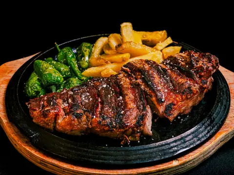Bistec a la parrilla con papas fritas y chile verde en plancha de hierro.