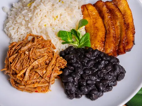 Plato con arroz, frijoles negros, carne mechada y plátano maduro.
