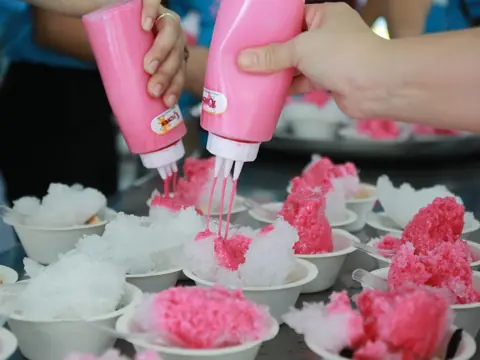 Sirope rosado cayendo sobre hielo granizado en vasos.