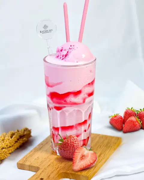 Batido rosado de fresa en vaso alto con fresas frescas.